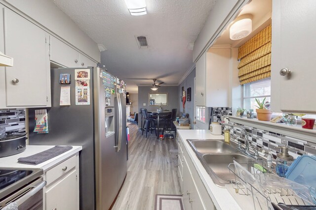 kitchen featuring sink, backsplash, a textured ceiling, white cabinets, and light wood-type flooring