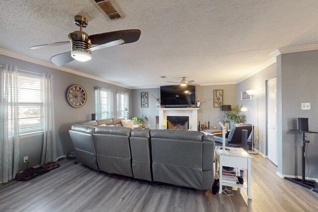 living room with wood-type flooring, ornamental molding, ceiling fan, and a textured ceiling