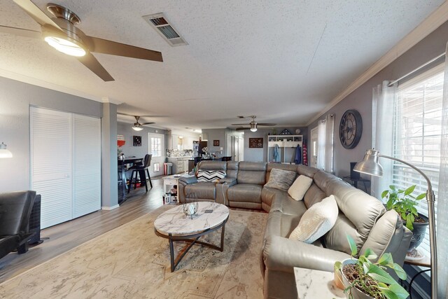 living room with ornamental molding, ceiling fan, a textured ceiling, and light hardwood / wood-style floors