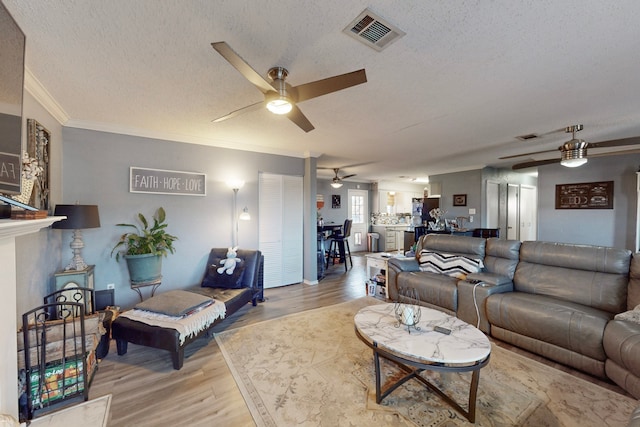 living room with ornamental molding, ceiling fan, a textured ceiling, and light wood-type flooring