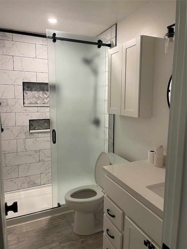 bathroom with hardwood / wood-style flooring, vanity, toilet, and a shower with shower door