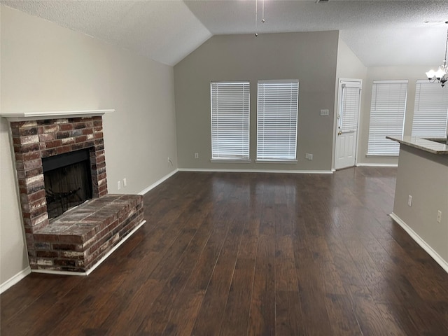 unfurnished living room featuring dark wood-type flooring, vaulted ceiling, a textured ceiling, a brick fireplace, and a notable chandelier