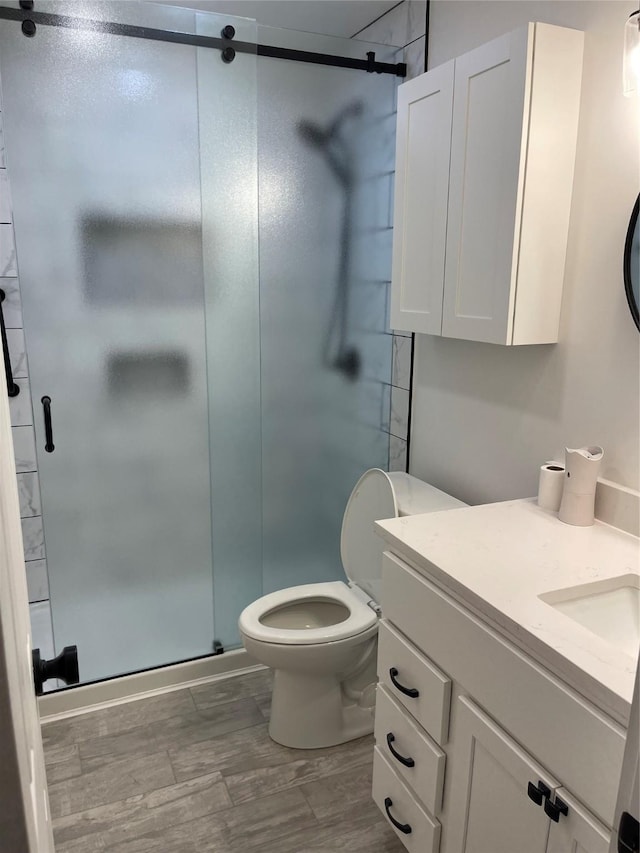 bathroom featuring hardwood / wood-style flooring, vanity, toilet, and a shower with shower door