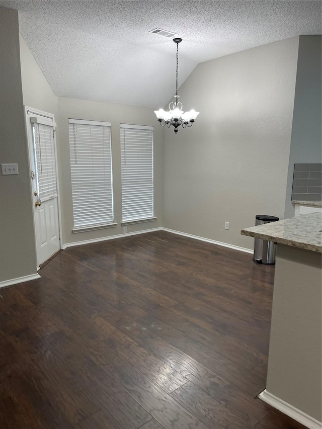 unfurnished dining area featuring an inviting chandelier, dark wood-type flooring, vaulted ceiling, and a textured ceiling