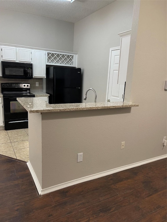 kitchen featuring white cabinetry, dark hardwood / wood-style floors, kitchen peninsula, light stone countertops, and black appliances