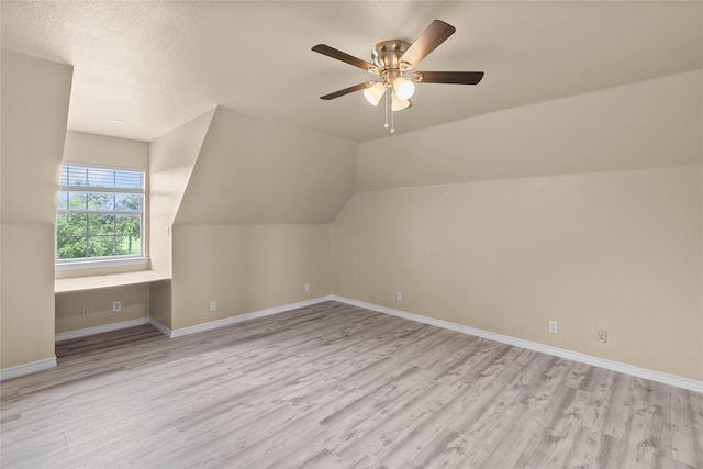 bonus room featuring ceiling fan, lofted ceiling, built in desk, and light wood-type flooring