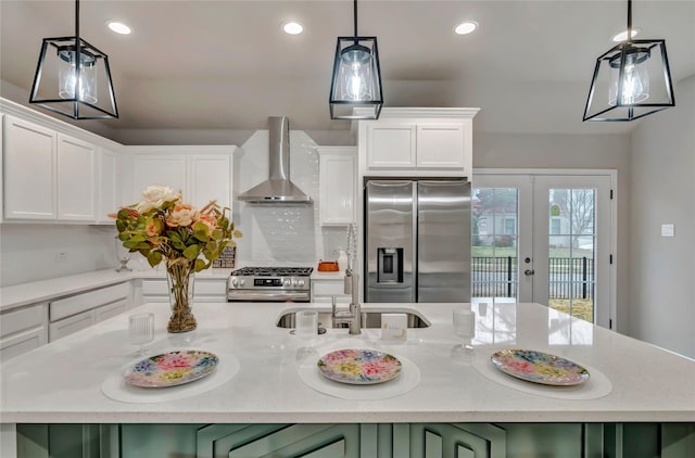 kitchen featuring wall chimney range hood, decorative light fixtures, stainless steel appliances, and white cabinets