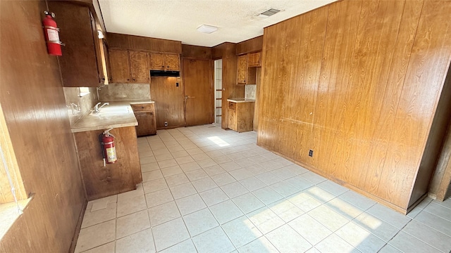 kitchen with sink, light tile patterned floors, a textured ceiling, and wood walls