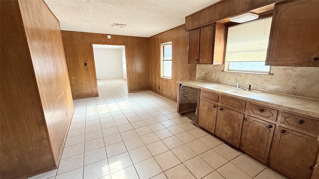 kitchen with dishwashing machine, sink, wooden walls, and a textured ceiling