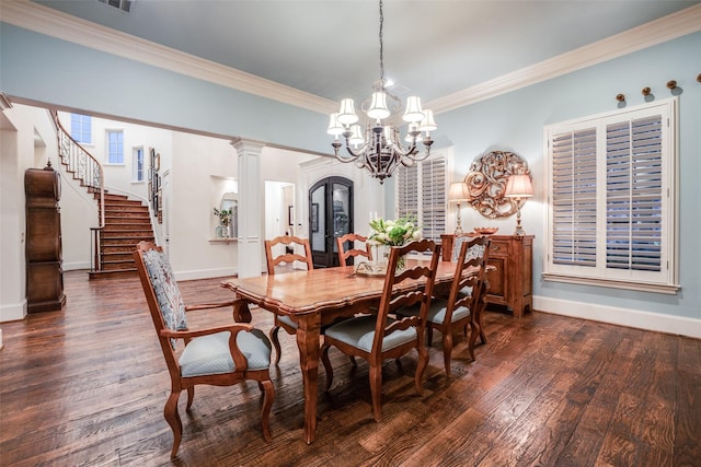 dining area featuring dark wood-type flooring, crown molding, ornate columns, and an inviting chandelier