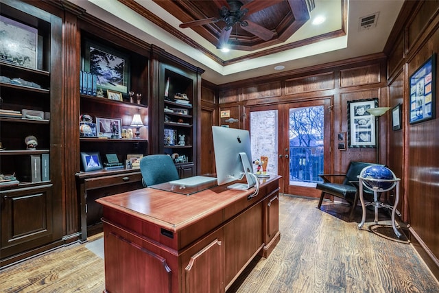 office space featuring light wood-type flooring, crown molding, a tray ceiling, ceiling fan, and wooden walls