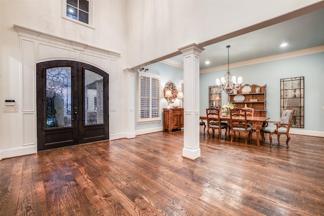 entryway featuring decorative columns, dark wood-style flooring, ornamental molding, french doors, and a notable chandelier