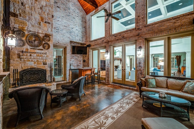 living area featuring ceiling fan, finished concrete flooring, a fireplace, high vaulted ceiling, and french doors
