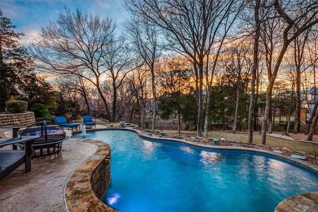 pool at dusk with a patio area, a fire pit, and pool water feature