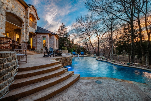 pool at dusk featuring a patio area, pool water feature, and an outdoor fire pit