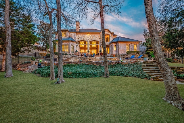 back of property featuring a lawn, fence, brick siding, and a chimney