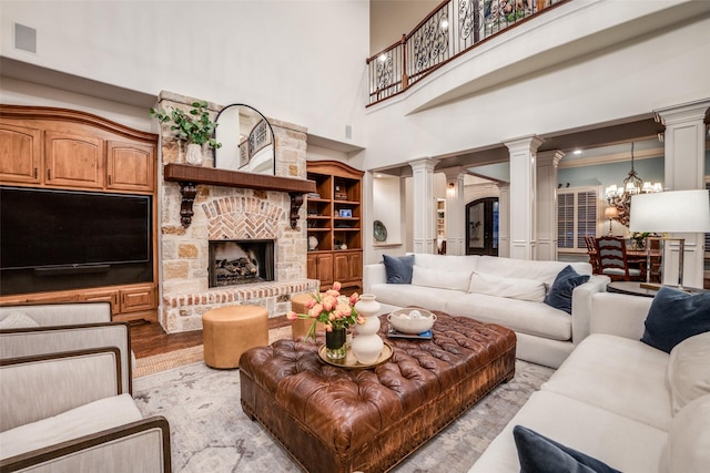 living room with decorative columns, a fireplace, a towering ceiling, light hardwood / wood-style flooring, and a chandelier