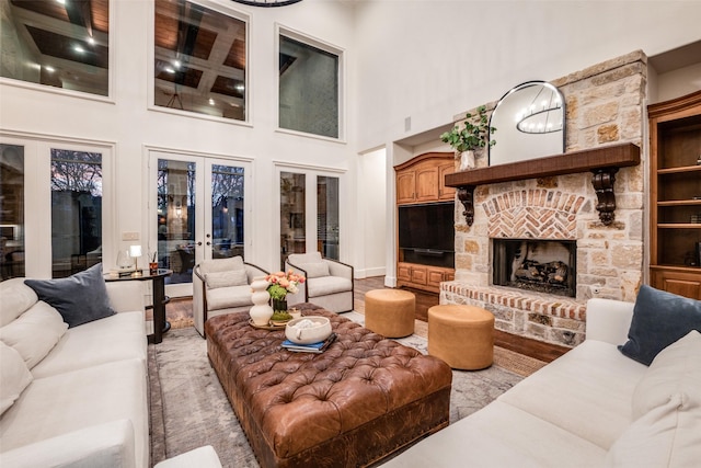 living room featuring french doors, wood-type flooring, a stone fireplace, and a high ceiling