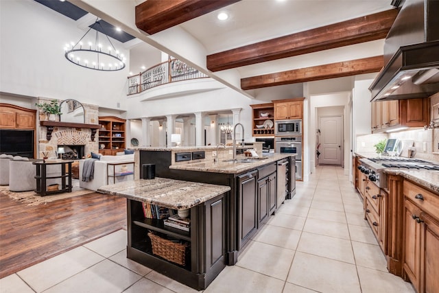 kitchen featuring a large island with sink, sink, light stone counters, appliances with stainless steel finishes, and island range hood