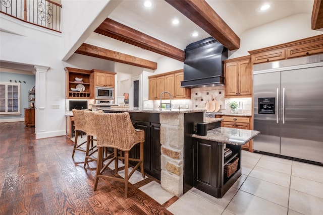 kitchen featuring light stone counters, open shelves, custom range hood, built in appliances, and beam ceiling