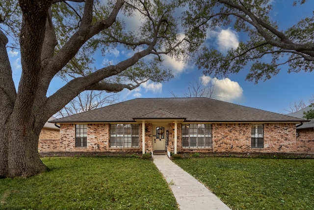 ranch-style home with a shingled roof, a front yard, and brick siding