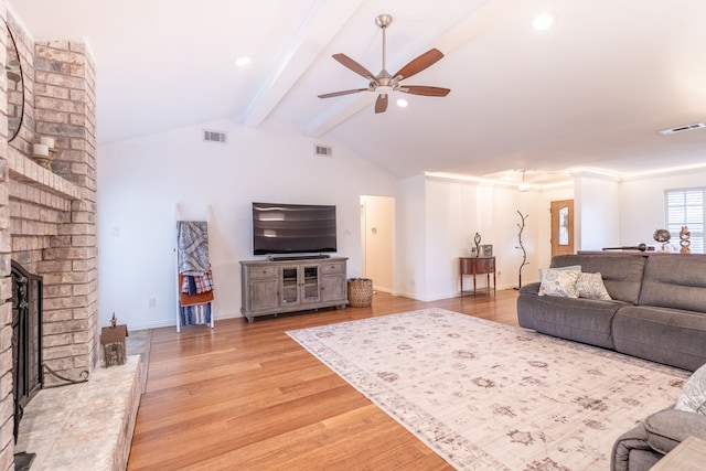 living room featuring a brick fireplace, lofted ceiling with beams, ceiling fan, and light wood-type flooring