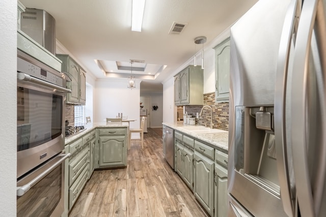 kitchen featuring appliances with stainless steel finishes, decorative light fixtures, sink, a tray ceiling, and light hardwood / wood-style flooring