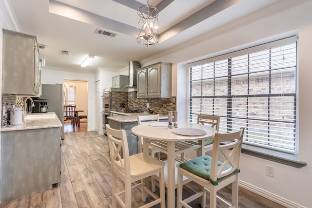 dining area with ornamental molding, a raised ceiling, and light wood-type flooring