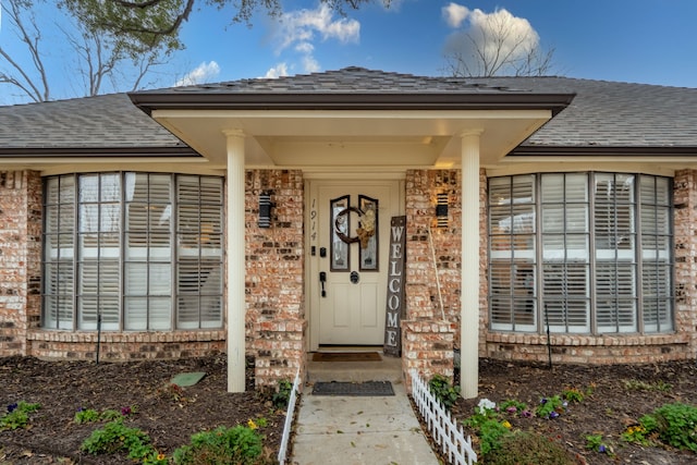 entrance to property featuring brick siding and roof with shingles