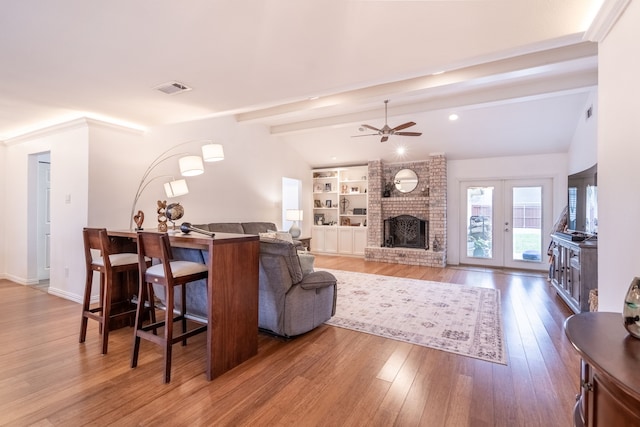 living room with built in features, wood-type flooring, vaulted ceiling with beams, a brick fireplace, and french doors