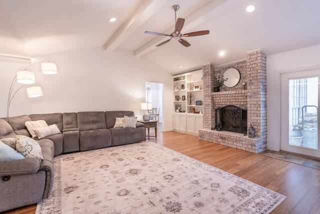 living room featuring ceiling fan, wood-type flooring, lofted ceiling with beams, and a brick fireplace