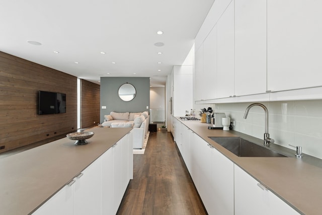 kitchen with wood walls, sink, white cabinets, stainless steel gas cooktop, and dark wood-type flooring