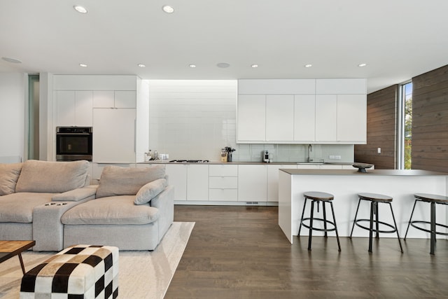 kitchen with sink, a breakfast bar, white cabinetry, backsplash, and stainless steel oven