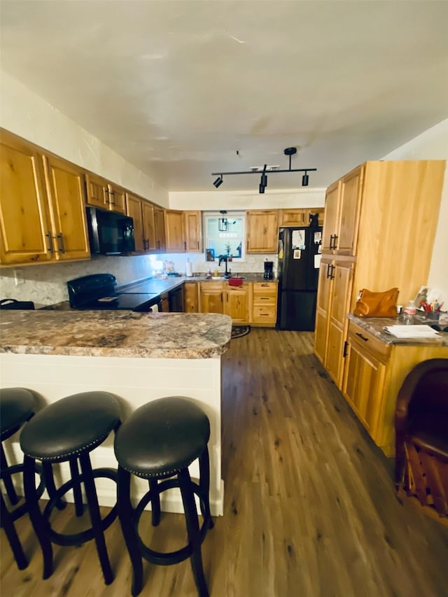 kitchen with a kitchen bar, dark hardwood / wood-style floors, kitchen peninsula, decorative backsplash, and black appliances