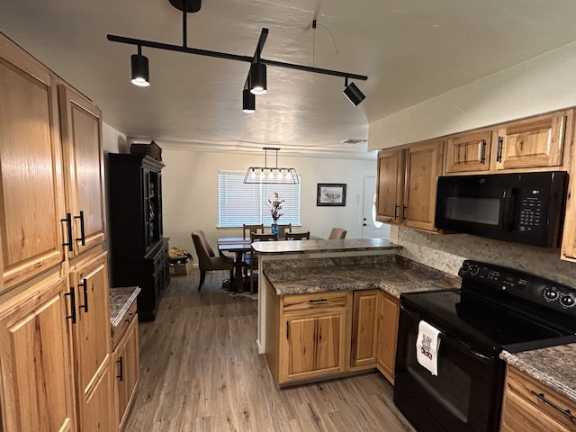 kitchen with pendant lighting, dark stone countertops, black appliances, kitchen peninsula, and light wood-type flooring