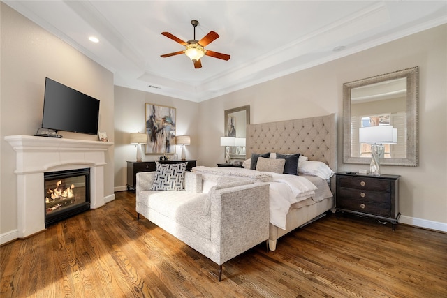 bedroom featuring dark wood-type flooring, ceiling fan, ornamental molding, and a tray ceiling