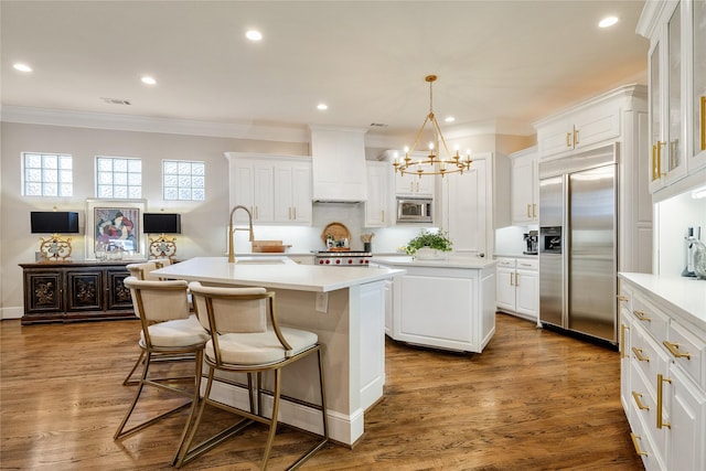 kitchen featuring sink, built in appliances, an island with sink, and white cabinets