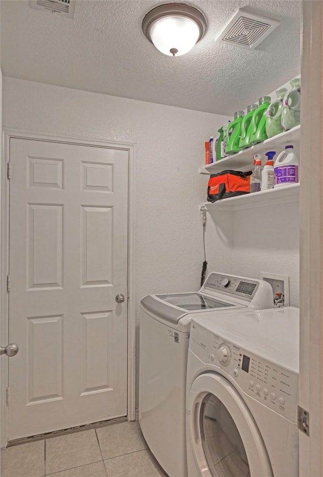 laundry area featuring separate washer and dryer, light tile patterned floors, and a textured ceiling