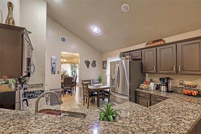 kitchen with dark brown cabinetry, lofted ceiling, sink, stainless steel fridge, and stone counters