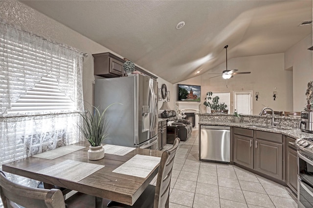 kitchen featuring lofted ceiling, sink, light stone counters, light tile patterned floors, and appliances with stainless steel finishes