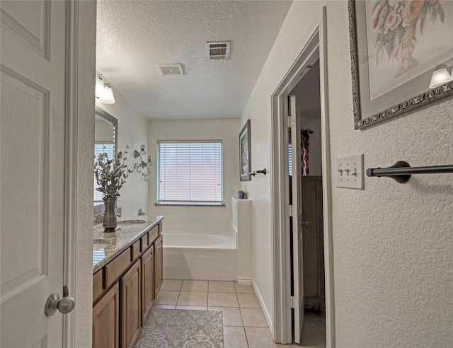 bathroom with tile patterned floors, a tub to relax in, a textured ceiling, and vanity