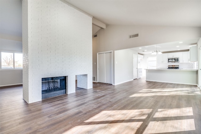 unfurnished living room with high vaulted ceiling, a notable chandelier, a fireplace, dark hardwood / wood-style flooring, and beamed ceiling