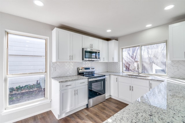 kitchen with stainless steel appliances, white cabinetry, sink, and light stone counters