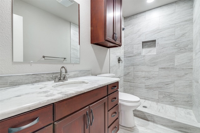 bathroom with vanity, toilet, and a tile shower