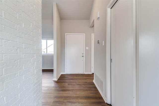 corridor with brick wall and dark hardwood / wood-style flooring