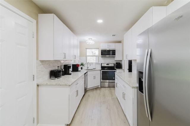 kitchen featuring white cabinetry, decorative backsplash, light stone countertops, and appliances with stainless steel finishes