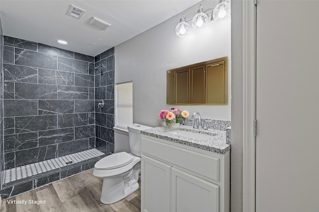 bathroom featuring wood-type flooring, a tile shower, vanity, and toilet