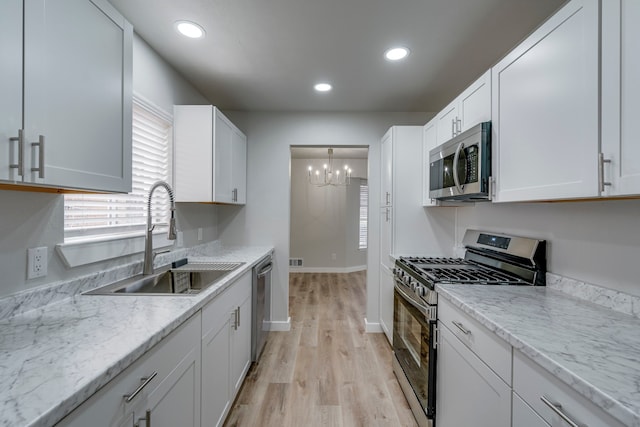 kitchen with stainless steel appliances, white cabinetry, light stone countertops, and sink