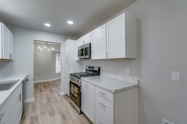 kitchen with appliances with stainless steel finishes, light stone counters, light hardwood / wood-style floors, white cabinets, and a chandelier