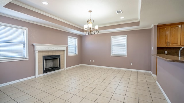 unfurnished living room with light tile patterned floors, a notable chandelier, ornamental molding, a tiled fireplace, and a raised ceiling